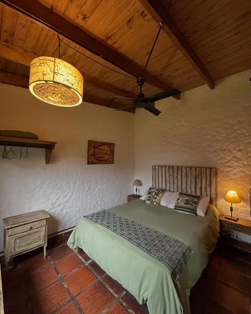 El dormitorio de El Ciruelo: cama doble con acolchado verde, techo de madera y lámpara de tela.