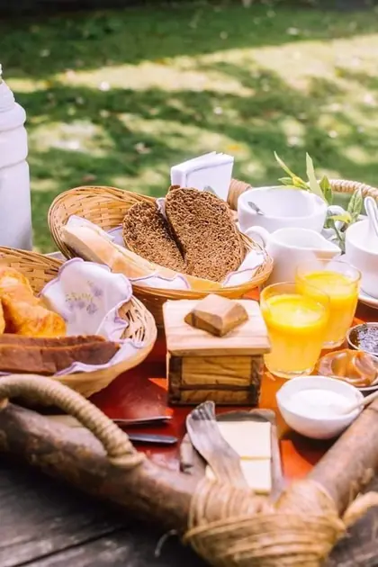 Bandeja de desayuno en el parque: pan casero, medialunas, jugo de naranja y café.