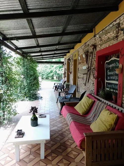 Galería con banco de madera, almohadones de colores y piso de baldosas.