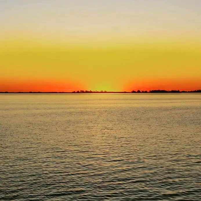 Atardecer sobre la laguna de Chascomús: el sol se pone en el horizonte y el cielo naranja se refleja en el agua.