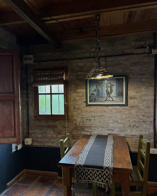 Mesa de madera con camino tejido, pared de ladrillo y una ventana pequeña.