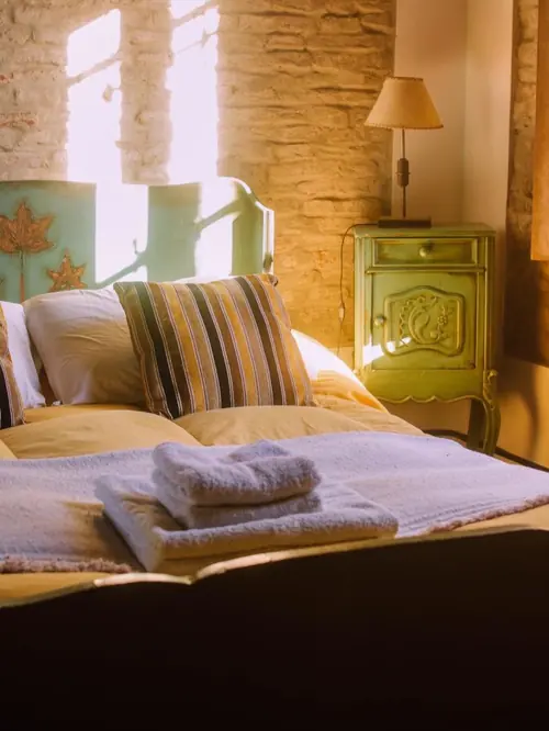 Cama con almohadones a rayas, toallas y una mesa de luz verde pintada a mano.
