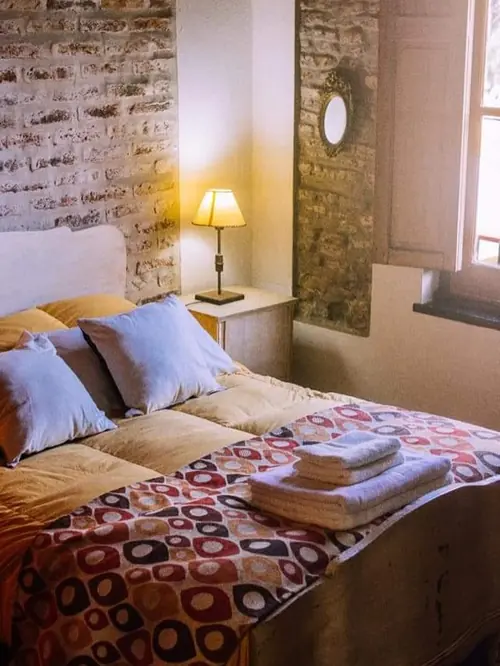 Suite con ladrillo, cama con manta estampada y una lámpara encendida.