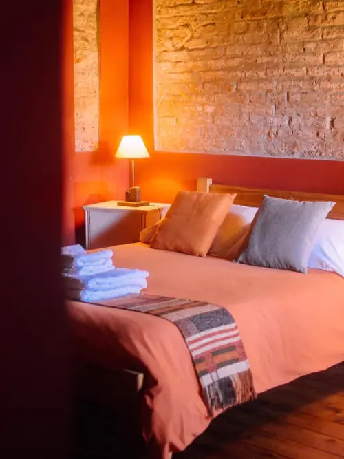 Suite con pared roja, ladrillo, cama con acolchado naranja y lámpara encendida.