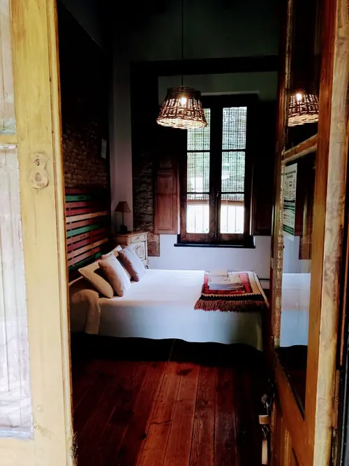 Suite con ventanal de madera, dos lámparas de mimbre y cama con manta a rayas.