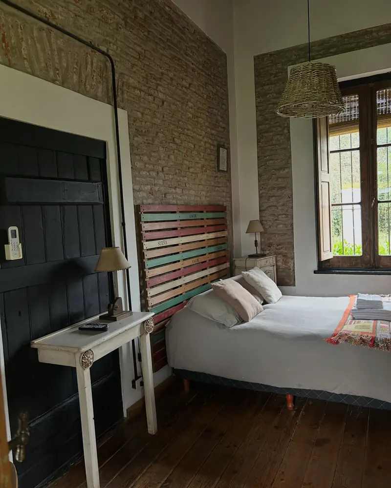 La habitación 8: cama doble con manta tejida, respaldo de maderas pintadas de colores y pared de ladrillo.
